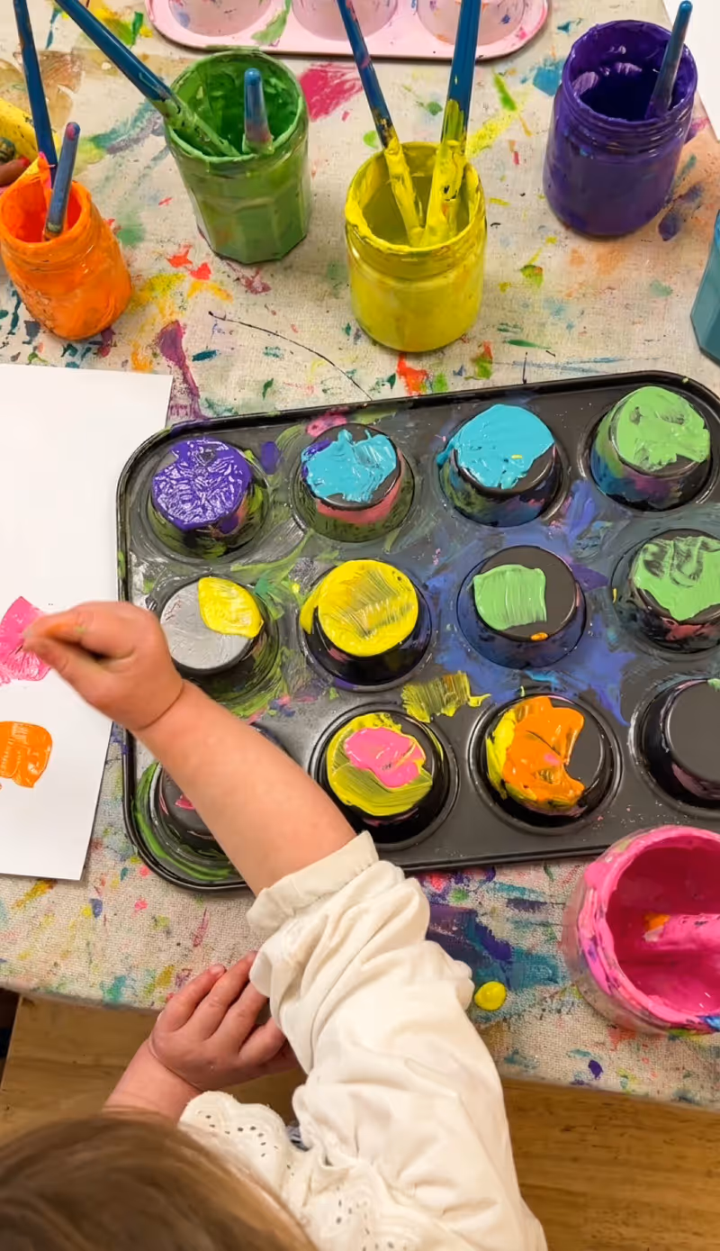 A muffin tray of bright paint pots ready for a holiday program day